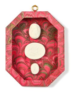 two soaps are sitting in a pink and gold tray on a white surface with an intricate design