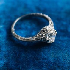 an antique style engagement ring on a blue velvet surface with the center diamond in the middle