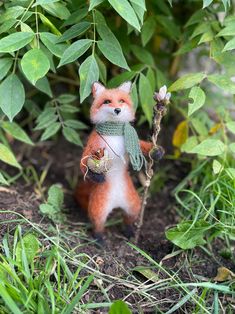 a small red fox figurine holding a stick in its mouth and wearing a scarf