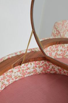 a mirror sitting on top of a pink chair next to a flower covered cushion with a chain hanging from it