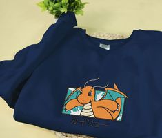 Introducing our Dragonite Embroidered Sweatshirt, the perfect gift for Christmas, birthdays, or any holiday celebration! Made with meticulous embroidery, this sweater showcases the majestic Dragonite in all its glory. The soft and cozy fabric ensures comfort while keeping you warm during the chilly winter months. With its vibrant colors and intricate design, this sweater is a true standout. Whether you’re a Pokémon enthusiast or looking for a unique present, our Dragonite Embroidered Sweat Blue Long Sleeve T-shirt With Embroidered Text, Casual Sweatshirt With Embroidered Graphics As Gift, Casual Long Sleeve T-shirt As Gift, Winter Gift Sweatshirt With Embroidered Graphics, Winter Sweatshirt With Embroidered Graphics As Gift, Blue Embroidered Fleece Sweatshirt, Winter Long Sleeve T-shirt With Embroidered Graphics, Custom Embroidered Long Sleeve Sweater, Fall Sweatshirt With Embroidered Graphics For Gift