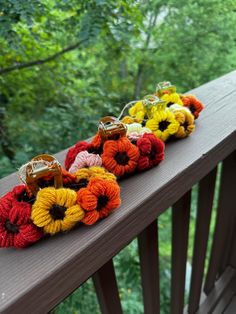 several crocheted flowers are lined up on a wooden rail in front of trees