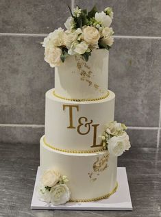 a three tiered wedding cake with white flowers and gold trimmings on top