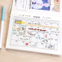 an open planner sitting on top of a wooden table next to a pen and paper