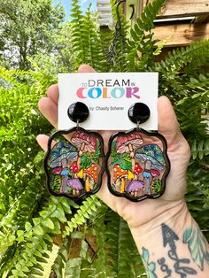 a person holding up two small earrings in front of some plants and trees with the words dream