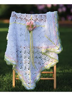 a crocheted shawl draped over a wooden chair in the grass with flowers on it