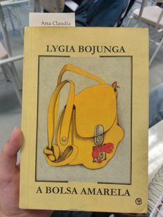 a person holding up a yellow book in their hand with an image of a purse on it