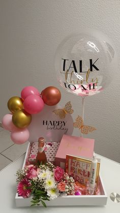 a birthday gift box with balloons, flowers and confetti on the table next to it