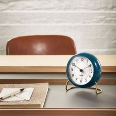 an alarm clock sitting on top of a desk next to a notepad and pen