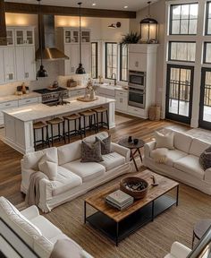 a large open concept kitchen and living room with wood flooring, white couches, coffee table, center island in the middle