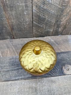 a gold vase sitting on top of a wooden table next to a wood plank wall