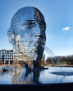 a large metal sculpture in the shape of a human head on top of a body of water