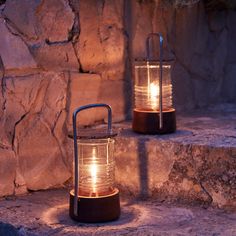 two lights that are sitting on some stone steps in front of a rock wall, one is lit up and the other is turned on