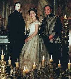 two men and a woman dressed in period costumes stand next to candles on a table