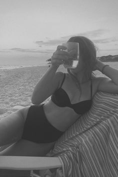 a woman laying on top of a beach next to the ocean taking a selfie