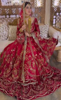 a woman in a red and gold bridal gown sitting on a couch with pillows