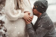 a man and woman standing in the snow holding each other's hands as they kiss