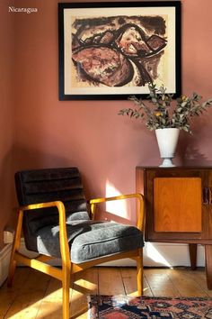 a living room with pink walls and a painting on the wall next to a chair