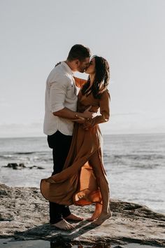 a couple kissing on the beach in front of the ocean during their engagement photo session