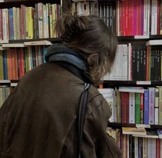 a woman is looking at books in a book store while wearing a brown leather jacket