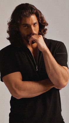 a man with long hair and a beard is posing for the camera while holding his hand to his mouth