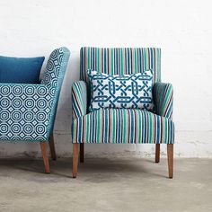 two chairs sitting next to each other in front of a white brick wall with blue and green designs on them