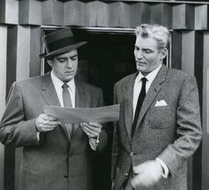 two men in suits are looking at something on a piece of paper while standing next to each other