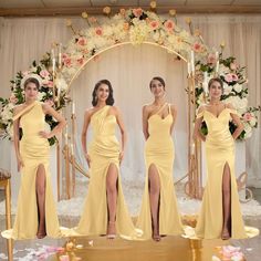 four women in yellow dresses standing on a stage with flowers and an archway behind them