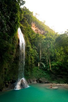 a large waterfall in the middle of a forest filled with green trees and people swimming