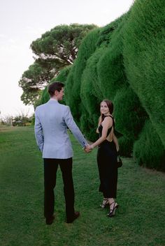 a man and woman are holding hands in front of some green bushes on the grass