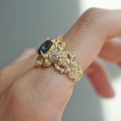 a woman's hand holding a gold ring with a blue stone in it and diamond accents