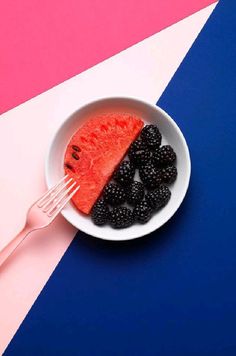 a white bowl filled with blackberries and raspberries on top of a pink and blue table