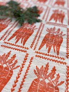 an orange and white table cloth with carrots on it next to a small plant