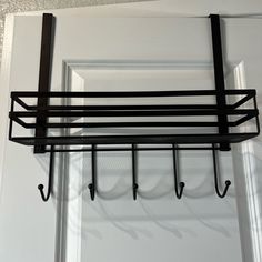 a black metal shelf with hooks hanging from it's sides on a white door