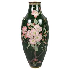 a green vase with pink flowers painted on the side and gold trim around the bottom