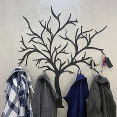 a coat rack with three coats hanging on it and a tree shaped metal wall art