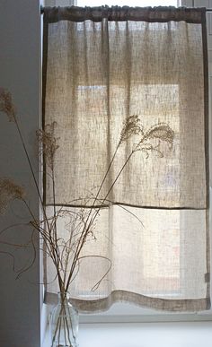 a vase filled with dried flowers sitting in front of a window sill next to a curtain