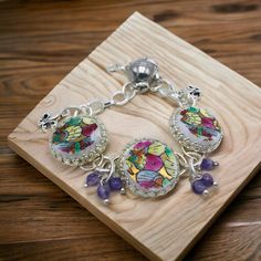 the bracelet is decorated with colorful glass beads and silver chains on a wooden board,