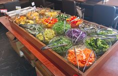 an assortment of food is displayed on a wooden table in a buffet style setting with glass bowls and utensils