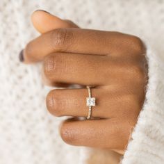 a woman's hand wearing a gold ring with a square shaped diamond on it