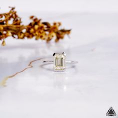 an emerald colored diamond sits on top of a white surface next to some dried flowers