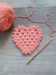 a crocheted heart next to a knitting needle and ball of yarn on a wooden surface