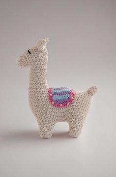 a crocheted llama is standing on a white surface and it has a blue, pink, green, and purple design on its back end