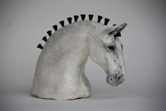 a white ceramic horse head with black spikes on it's ears and nose, against a gray background