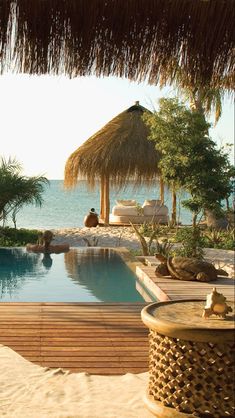 an outdoor swimming pool with thatched umbrellas next to the water and people lounging