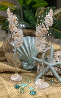 two wine glasses sitting on top of a table next to shells and seashells