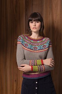 a woman standing with her arms crossed in front of a wooden wall wearing a colorful sweater