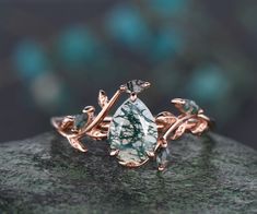 a green and white stone ring sitting on top of a piece of rock with leaves around it