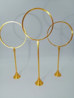 three gold colored metal circles on stands with one standing and the other holding two rings