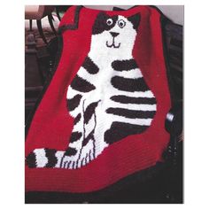 a knitted cat sitting on top of a red blanket with black and white stripes